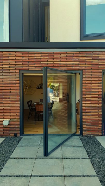 Pivot Line glass door open against a brick facade