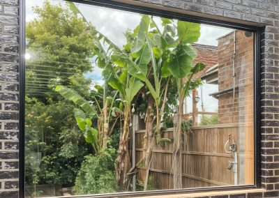 Large fixed aluminium window in a black brick wall